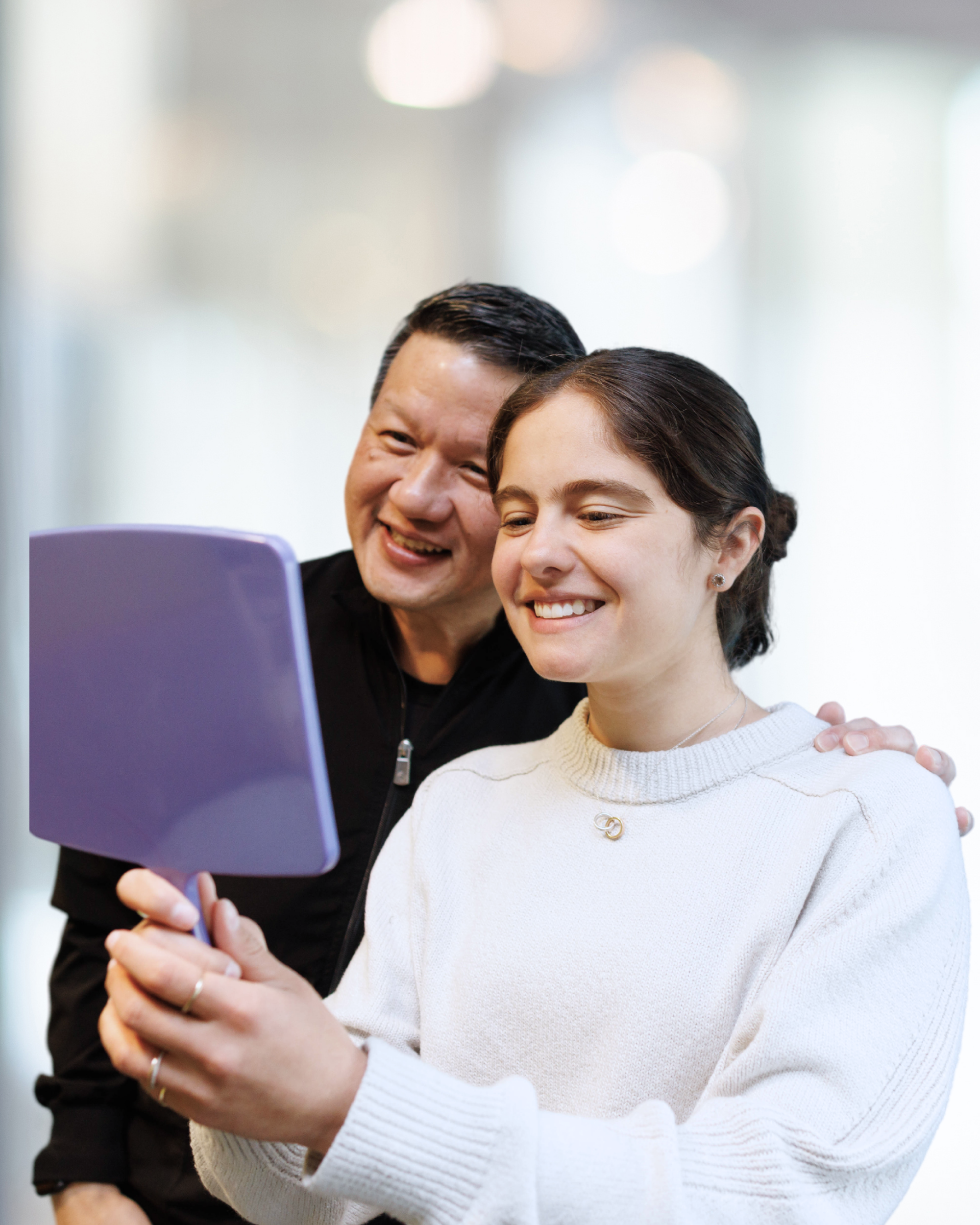 Smiling young woman looking at her teeth in a purple handheld mirror beside a man