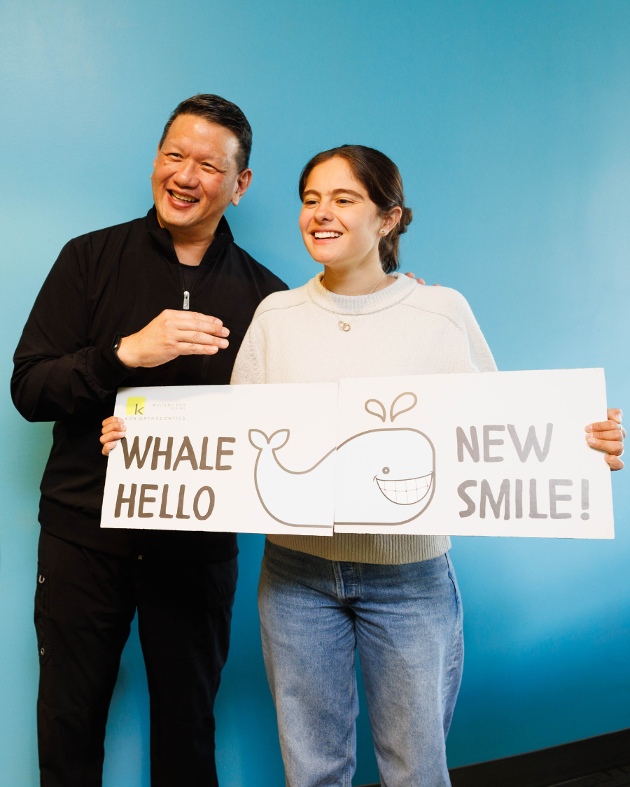 Smiling man and young woman holding whale sign reading "Whale Hello New Smile!"